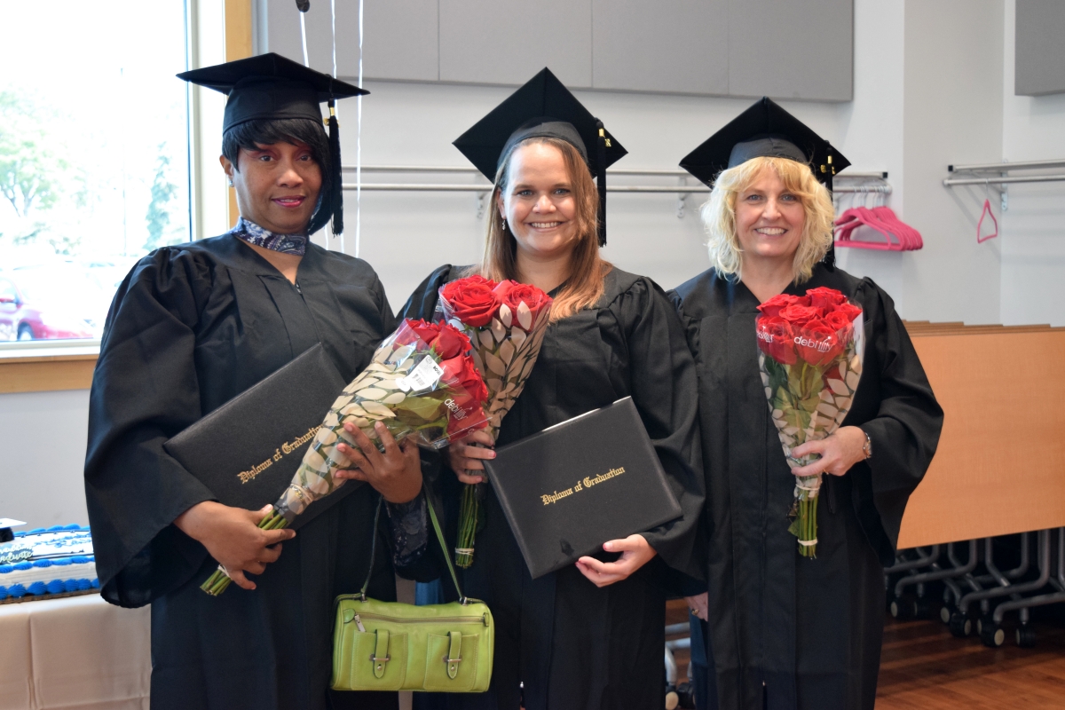 Photo of 3 graduates holding their diplomas and flowers