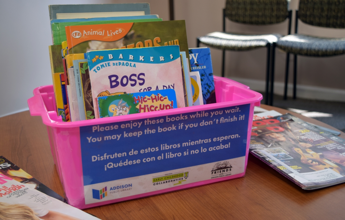 Photo of book bin sitting on table. The bin is filled with children's books. 