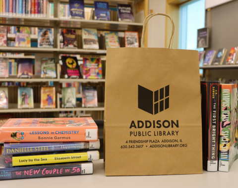 photo of brown paper bag with addison public library logo and address on it next to a stack of books