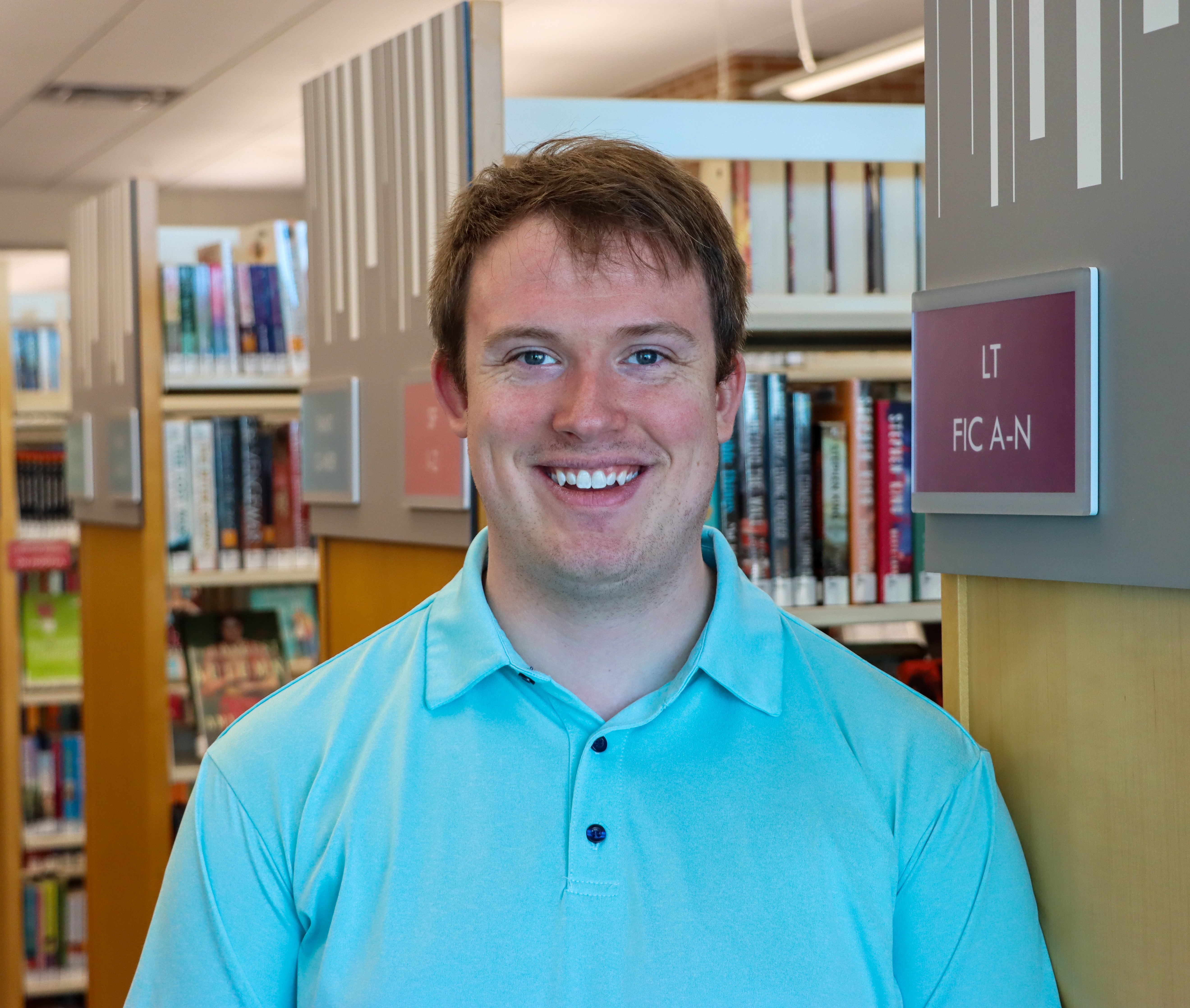 white man with blue polo standing in library bookstacks