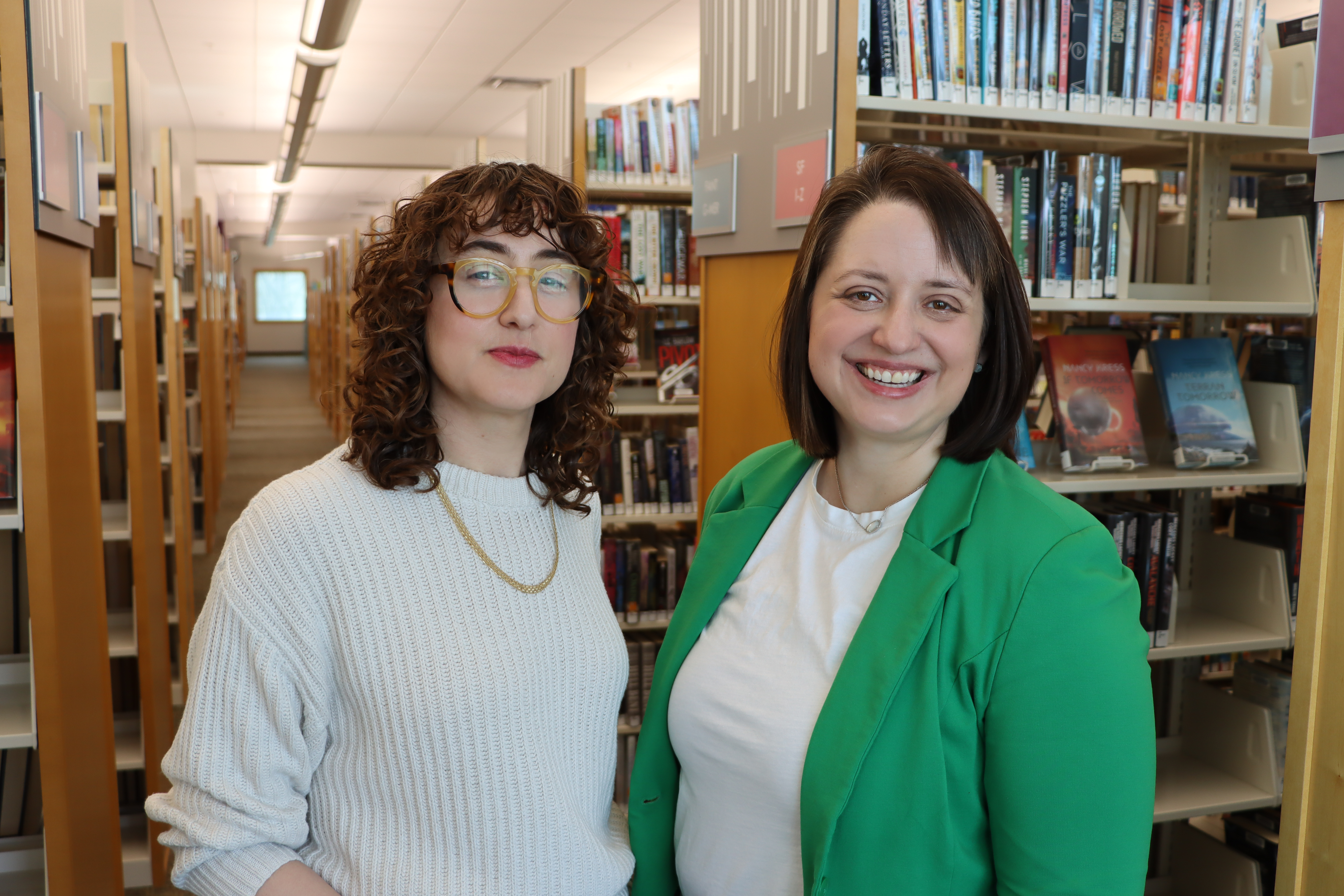 two women stand in front of bookshelves