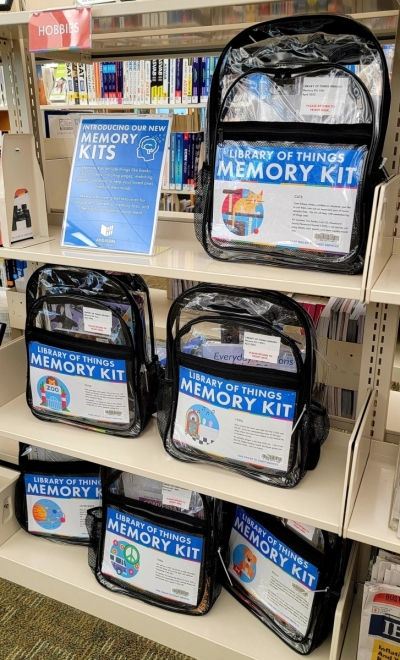 Photo of Memory Kits on the shelf. Memory Kits are assembled in clear backpacks and include a mix of books, DVDs, music, activities, or games.