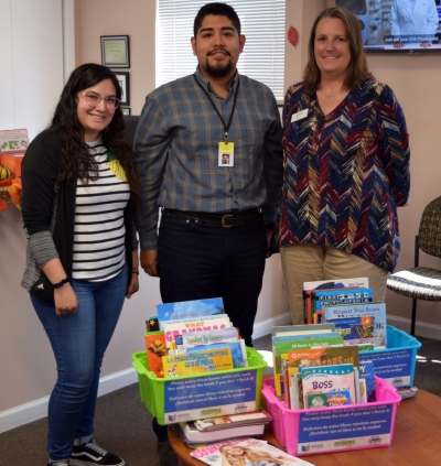 Photo of Kathy Welko (Head of Community Engagement) standing next to two Hamdard Health employees with book bins