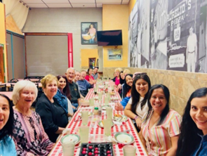 Group of people sitting at long dinner table smiling at camera 