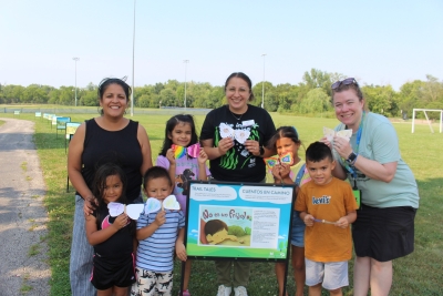 Group of people holding their moth craft around a storyboard in the park.