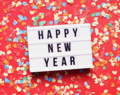 white box with letters spelling HAPPY NEW YEAR laying on red background with colorful paper confetti