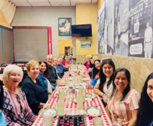 Group of people sitting at long dinner table smiling at camera 