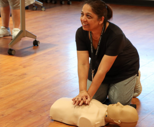 photo of woman kneeling next to a cpr dummy and performing hands-only cpr