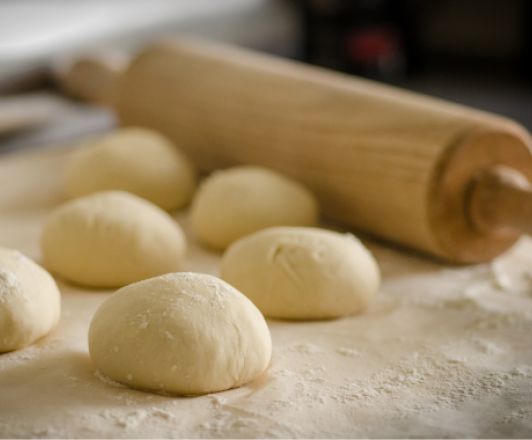 wooden rolling pin and dough balls on a kitchen counter