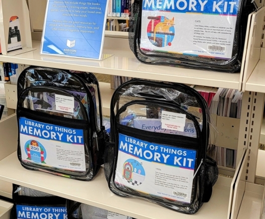 Photo of Memory Kits on the shelf. Memory Kits are assembled in clear backpacks and include a mix of books, DVDs, music, activities, or games.