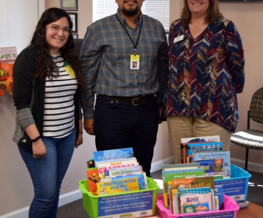 Photo of Kathy Welko (Head of Community Engagement) standing next to two Hamdard Health employees with book bins