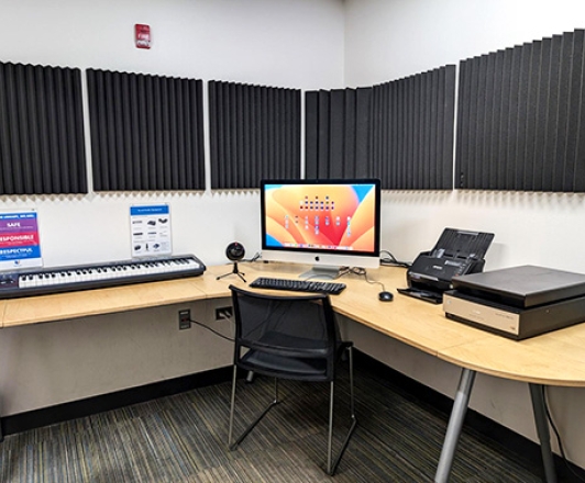 Photo of Sound Studio. The Sound Studio is a small room with a table and iMac. On the table is a piano keyboard, microphone, flatbed scanner, and document feeder.