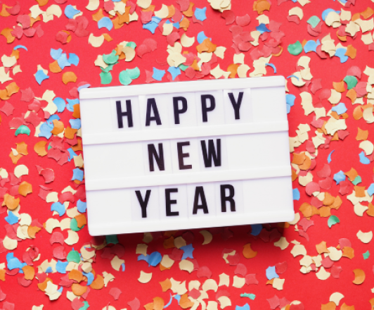 white box with letters spelling HAPPY NEW YEAR laying on red background with colorful paper confetti