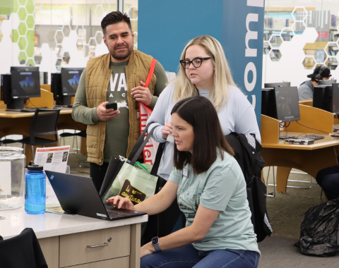 one seated woman on laptop assistant two standing people at desk