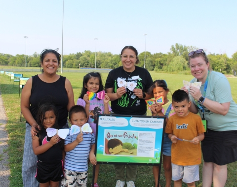 Group of people holding their moth craft around a storyboard in the park.